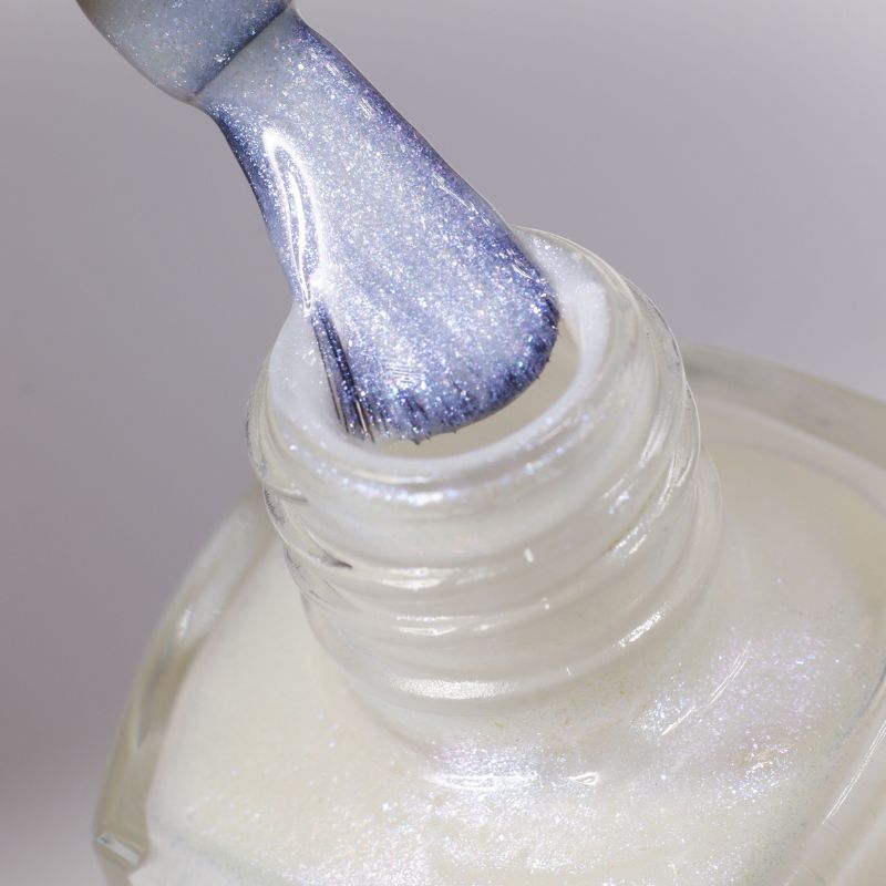 Close-up of a nail polish brush with metallic lavender color being lifted from a glass bottle.
